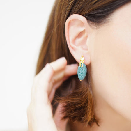 Woman wearing sky blue volcanic drop earrings made with natural volcanic stones and 18K gold-plated over sterling silver.